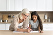 © fizkes - Happy senior grandmother and preteen age kid granddaughter spend leisure time together enjoy drawing colorful pictures in album on kitchen table. Caring granny help cute girl to do creative homework