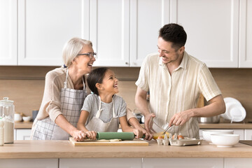 Wall Mural - Family recipe. Happy friendly 3 diverse generations relatives old grandma young adult dad little preteen child girl spend funny leisure time at modern house kitchen doing chores cooking pie for lunch