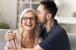 © fizkes - Touching care. Affectionate grateful young adult son embrace smiling elder age retired mother in glasses give mum tender kiss in living room express love sincere gratitude for kindness understanding