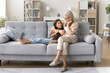 © fizkes - Granny is my trusted person. Happy little girl junior schoolchild relax on comfy couch at living room in caring embraces of loving mid aged grandma talk share secrets ideas plans feel bonding support