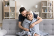 © fizkes - Let me take care of you. Caring attentive grown up millennial man son wrapping shoulders of grateful mom sit resting on sofa with warm woolen blanket protect loved parent from cold at cool living room