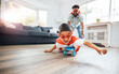 © peopleimages.com - Father, child and superhero costume in home for flying on skateboard or playing fantasy games together. Dad, boy and happy kid in cosplay character mask for bonding in living room in family house