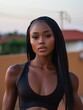 © Matt - Close-up portrait of a beautiful African woman with long hair, wearing a black sports bra, standing outdoors in front of a blurred background of a residential area