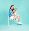 © sitthiphong - Songkran festival in Thailand, Happy smiling young Asian woman in summer sit in deckchair and holding water guns in blue background.