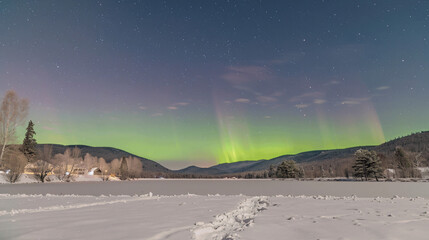 Aurora borealis above mountains in fog at night. Northern lights. Sky with stars with polar lights and high rocks. Beautiful landscape with aurora, city lights in low clouds, mountain ridge. Space