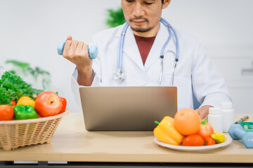 Wall Mural - An Asian male nutritionist with a beard, wearing a lab coat, sits at a desk for an online consultation. His workspace includes fruits, vegetables, laptop, health supplements, promoting wellness.