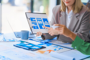 A young African American woman and a young Russian woman work together in a business office. They discuss UX design, using color swatches and tablets, while planning layouts and interfaces.