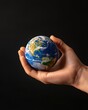 © Somporn - A hand holds a small globe, symbolizing care for the Earth, against a dark background.
