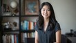 © OS - Young Asian female translator smiling during consultation with books and globe in background in cozy office.  Language consultant, professional service, office consultation, cultural understanding,