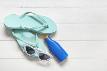 Wall Mural - Bottle of sunscreen cream, sunglasses and flip-flops on light wooden background