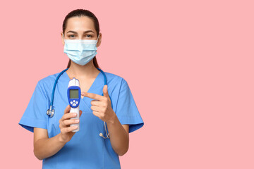 Poster - Portrait of female doctor in mask pointing at infrared thermometer on pink background