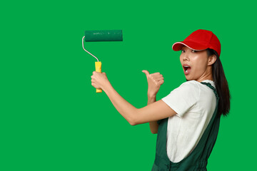 Wall Mural - female asian shocked painter pointing at roller on green background