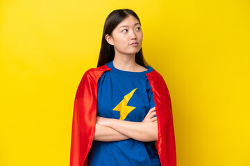 Wall Mural - Young Chinese woman isolated on yellow background in superhero costume with arms crossed