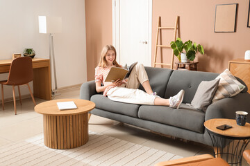 Wall Mural - Young pretty woman reading magazine on sofa in stylish living room