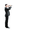 © peshkova - Side view of a businessman in a suit holding a telescope, standing against a white background. Concept of vision, future, and business outlook