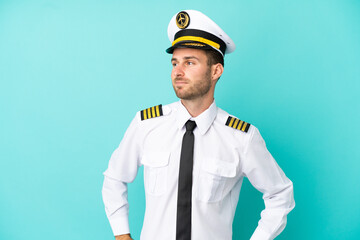 Wall Mural - Airplane caucasian pilot isolated on blue background posing with arms at hip and smiling