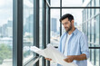 © Summit Art Creations - Professional architect engineer or male worker in casual outfit looking at skyscraper and city view while holding project plan. Creative design, civil engineering, building construction. Tracery.