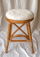 Canvas Print - Elegant wooden stool with quilted white cushion on soft fabric backdrop