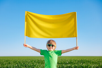 Wall Mural - Child holding yellow banner in spring green field