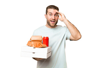 Wall Mural - Young handsome blonde man holding pizzas and burgers over isolated background with surprise expression