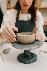Poster - Creating ceramic crockery in the workshop. Craftswoman carefully molds a clay bowl on the potters wheel.