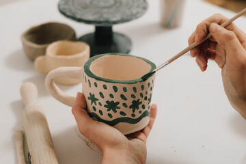 Poster - Artist is making decoration on the clay ceramic mug after oven firing. Design earthenware cup with a traditional pattern.