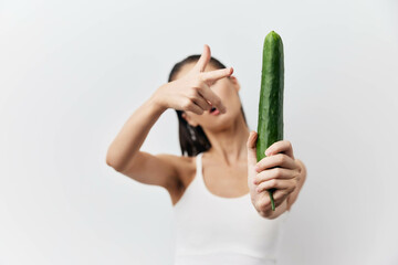 Wall Mural - Woman holding a cucumber in a playful manner against a bright white background, conveying humor and fun in food related contexts