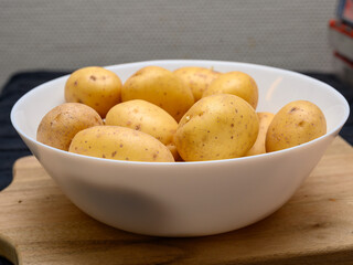 A collection of freshly harvested golden potatoes arranged in a white bowl rests on a wooden cutting board, showcasing their natural textures and earthy tones