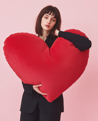 Wall Mural - A woman in black business attire holds an oversized, red heart-shaped handbag with a handle, standing against a white background.Minimal creative Valentine's fashion concept with copy space.