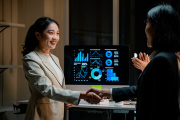 Wall Mural - Two businesswomen shaking hands after successfully presenting financial analysis data on a computer screen