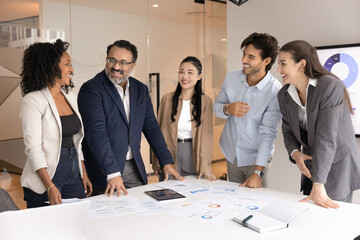 Wall Mural - Happy multiethnic coworkers of different ages discussing creative ideas, project marketing strategy at meeting table with sales reports, brainstorming, laughing, enjoying teamwork, training