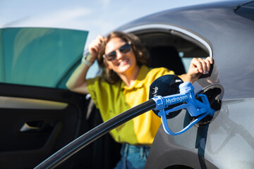 Wall Mural - Woman with fueling hydrogen car. Refueling car with hydrogen fuel. Wind turbines in the background