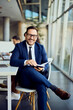© bnenin - Cheerful Businessman Seated Indoors in a Modern Office Environment Holding a Notebook