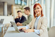 © bnenin - Professional Woman Smiling in Office Environment with Colleagues in Background
