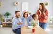 © Studio Romantic - Young happy parents mother, father and two children having fun together at home playing and throwing tennis balls into cardboard cup. Family and leisure concept.