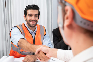 Diverse group of civil engineer and client shakes hand after make successful agreement on architectural project, reviewing construction plan and building blueprint at meeting table. Prudent