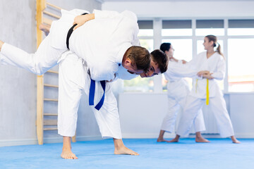 Wall Mural - Adult man and young guy in kimonos train judo techniques in group in studio..