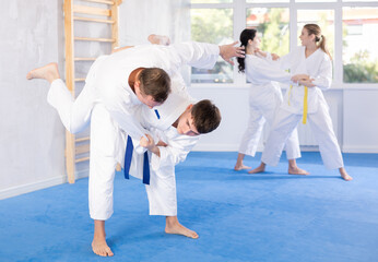 Wall Mural - Adult man and young guy in kimonos train judo techniques in group in studio..