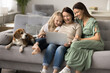© fizkes - Pretty multigenerational relatives women spend weekend leisure on sofa with dog using modern laptop, do e-shopping at home, watching movie via digital online subscriptions platforms. Family pastime