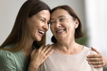 Wall Mural - Close up portrait two beautiful different generation women, daughter and mother smiling warmly looking at each other with love and tenderness, hugging indoor. Happy family, ties, bond, understanding