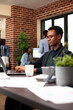 © DC Studio - Black businessman seated at desk, using his digital device to reply to work emails and review daily tasks. Male entrepreneur typing on his laptop, preparing startup business project in modern office.