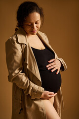 Pregnant woman embracing her belly and smiling against a soft warm background