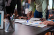 © DC Studio - Closeup of multiethnic group of people standing at table and reading financial paperwork. African american and caucasian individuals reviewing company documents on desk at startup office.