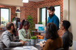 © DC Studio - Caucasian manager holding tablet and showing financial graphs to his team seated at table in brick wall office. Bearded businessman using digital device, explaining company growth to his colleagues.