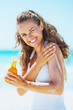 © Alliance - Smiling young woman applying sun block creme on beach