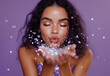 © RookStock - Glamorous woman blowing sparkling glitter against purple background in beauty concept