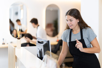 Wall Mural - Young female hairdresser stylist stands at cash register in beauty salon