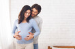 © Prostock-studio - Happy couple expecting baby and hugging near window at home, empty space
