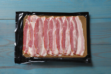 Wall Mural - Pack of sliced bacon on light blue wooden table, top view