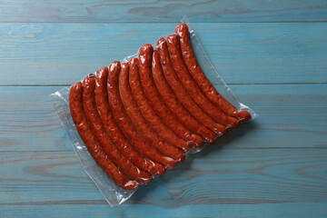 Wall Mural - Pack of dry smoked sausages on light blue wooden table, top view